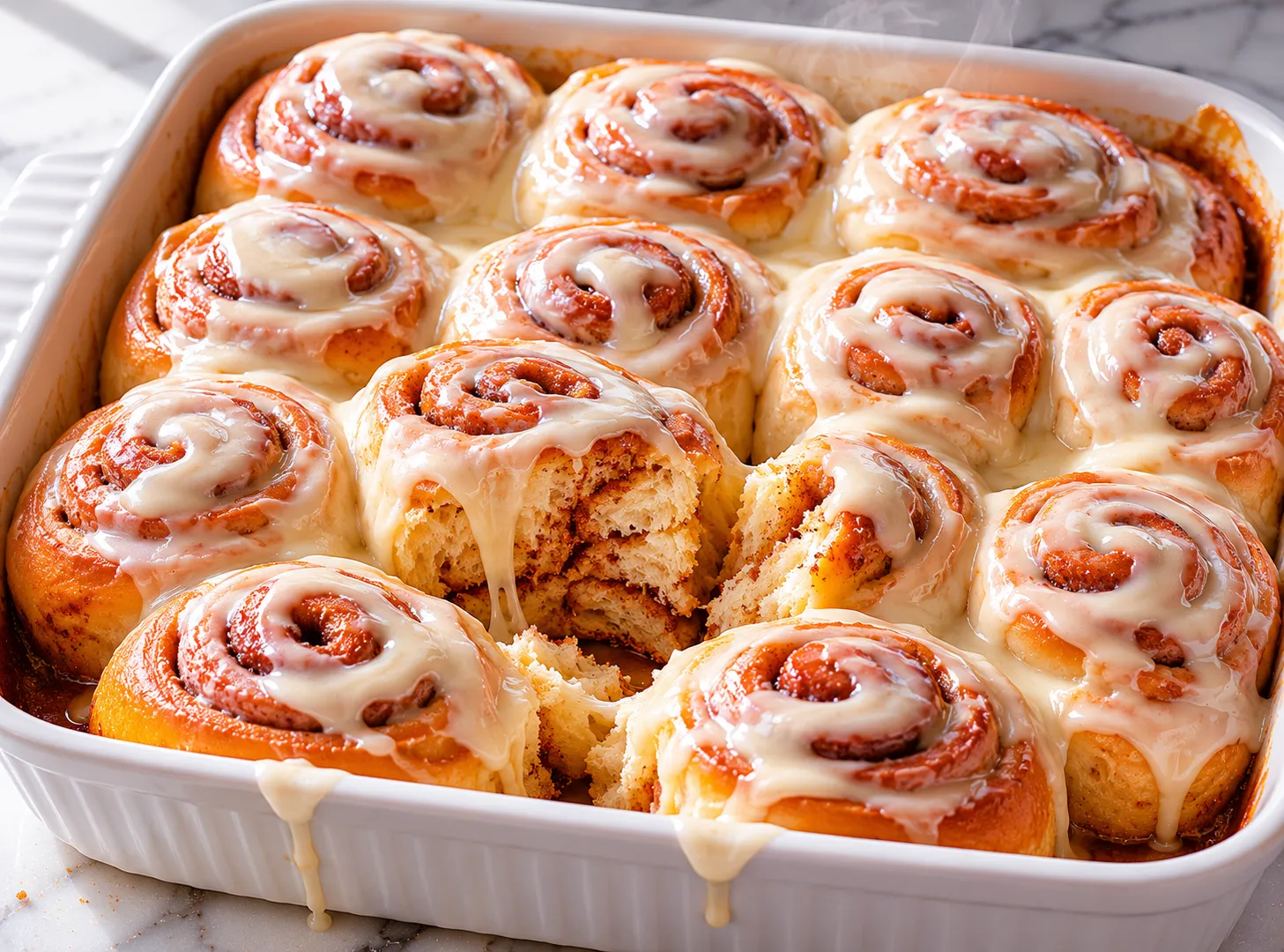 Freshly baked soft cinnamon rolls in a white baking dish covered with thick cream cheese glaze on a marble surface